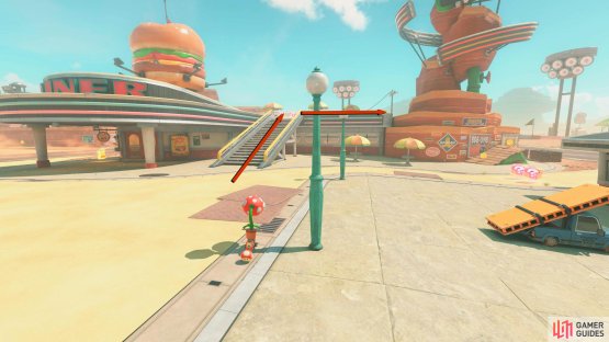 To the left of the flag is a small complex. Go up the stairs of the Diner and use the rails to the right to go around the building.